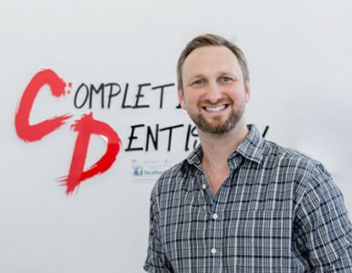 Headshot of male dentist in front of business logo